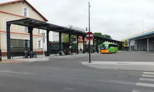 Zielony autobus FlixBus na przystanku autobusowym z wiatą i ławkami, gdzie siedzą pasażerowie.
