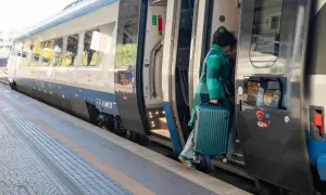 Kobieta z walizką wsiada do pociągu Pendolino na peronie.