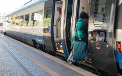 Kobieta z walizką wsiada do pociągu Pendolino na peronie.