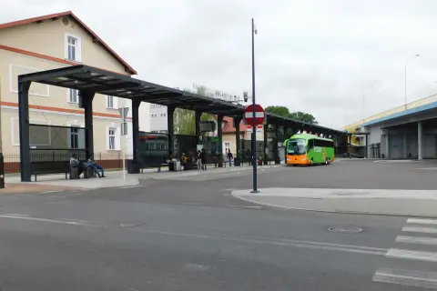 Zielony autobus FlixBus na przystanku autobusowym z wiatą i ławkami, gdzie siedzą pasażerowie.