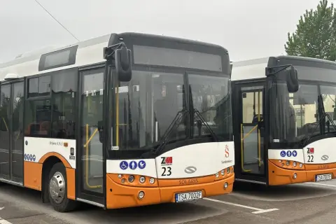 Dwa autobusy miejskie marki Solaris w kolorach białym i pomarańczowym, zaparkowane na placu.
