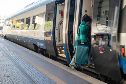 Kobieta z walizką wsiada do pociągu Pendolino na peronie.