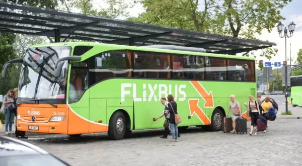 Zielony autobus Flixbus z pasażerami i bagażami na przystanku.