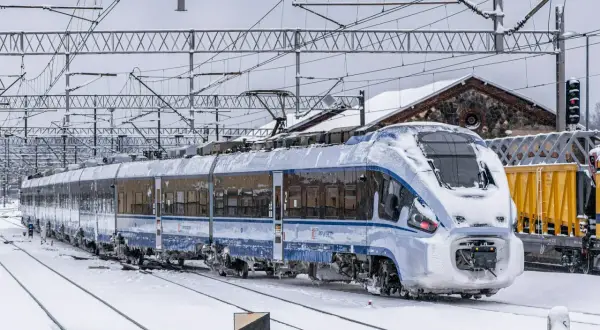 Pociąg PKP Intercity pokryty śniegiem na tle zimowego krajobrazu.
