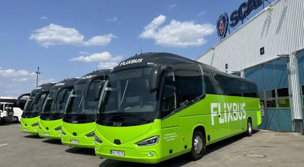 Rząd zielonych autobusów Flixbus zaparkowanych przed budynkiem z logo Scania.