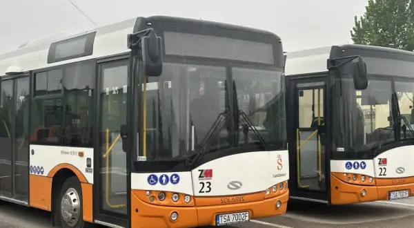Dwa autobusy miejskie marki Solaris w kolorach białym i pomarańczowym, zaparkowane na placu.