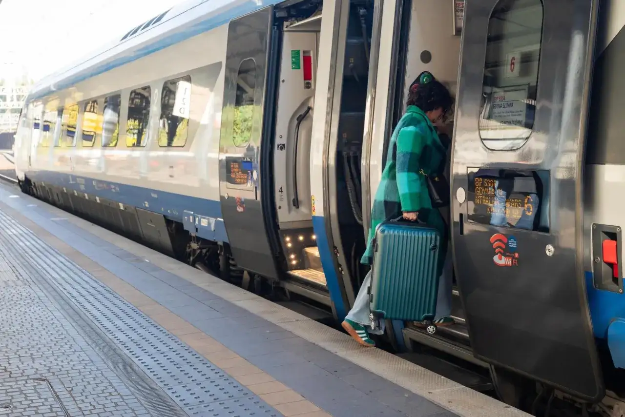 Kobieta z walizką wsiada do pociągu Pendolino na peronie.