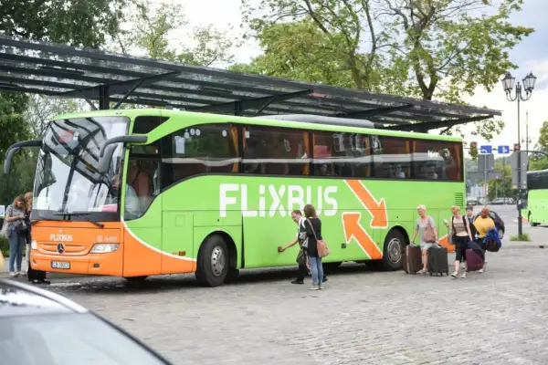 Zielony autobus Flixbus z pasażerami i bagażami na przystanku.